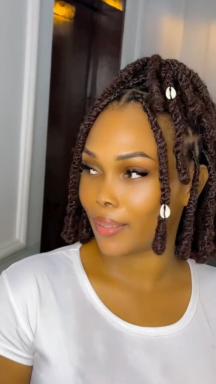 Woman with short brown hair twists adorned with small white cowrie shell beads.