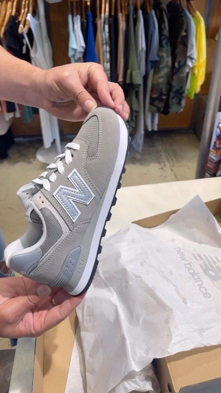 Grey New Balance sneaker with white sole held over a cardboard shoebox