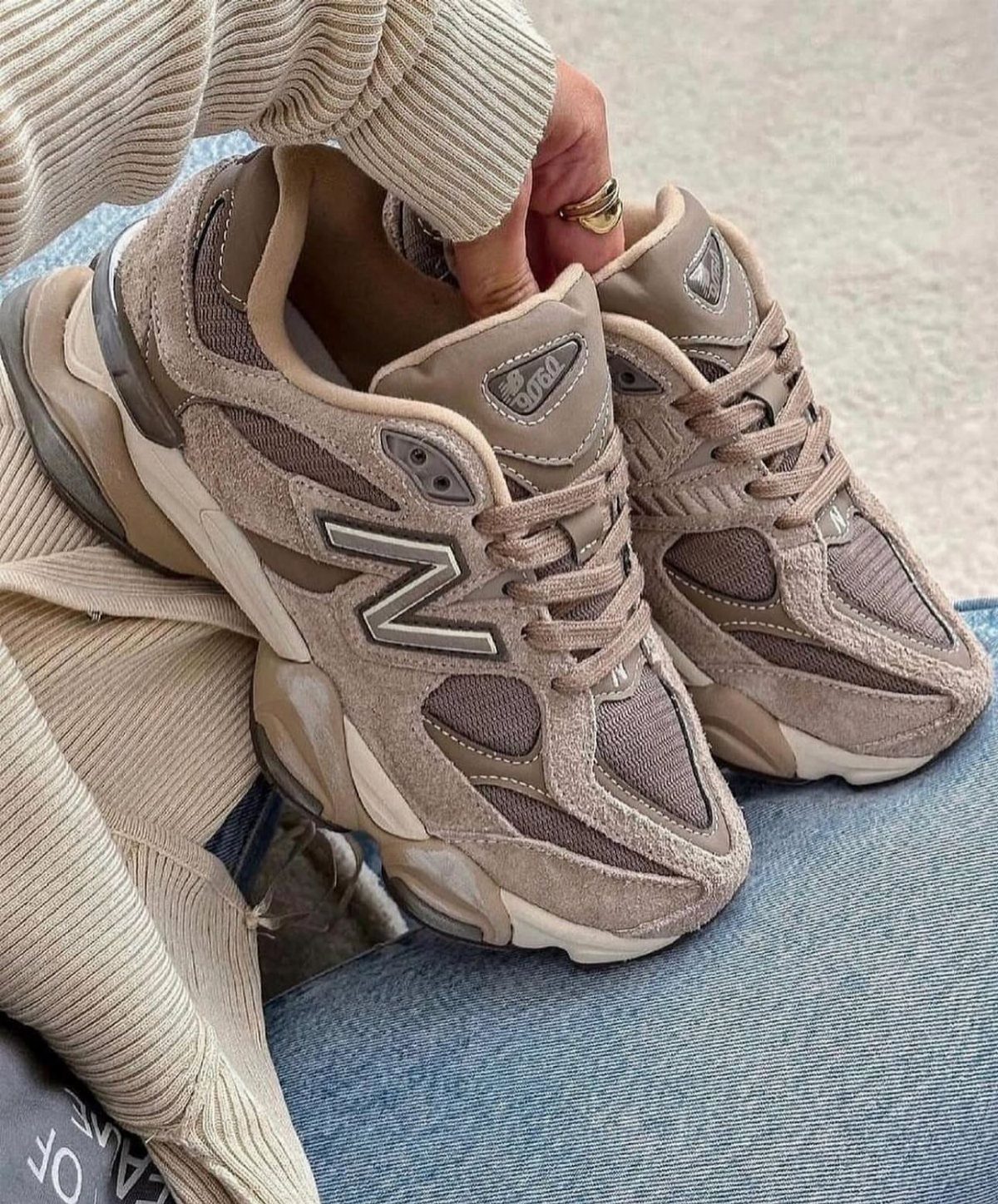 Neutral beige New Balance sneakers worn with blue jeans and a beige sweater.