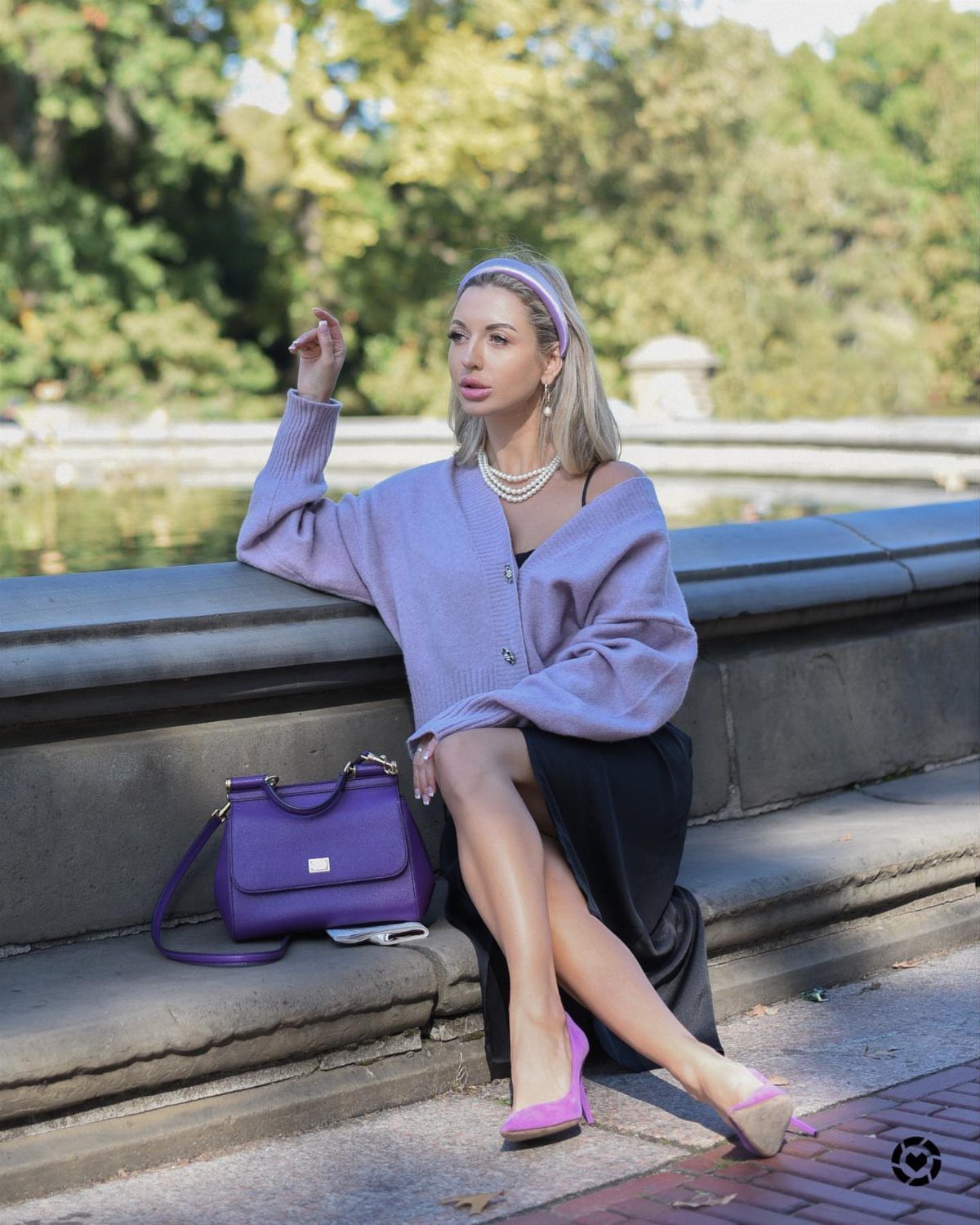 Woman in a purple cardigan and black slip dress sitting on a stone ledge.