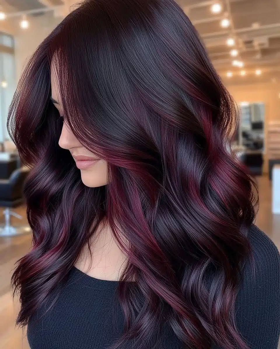 Oxblood Hair Color Ideas: 5 Looks for Every Length 3 Woman with long wavy oxblood red hair posing in a bright salon.