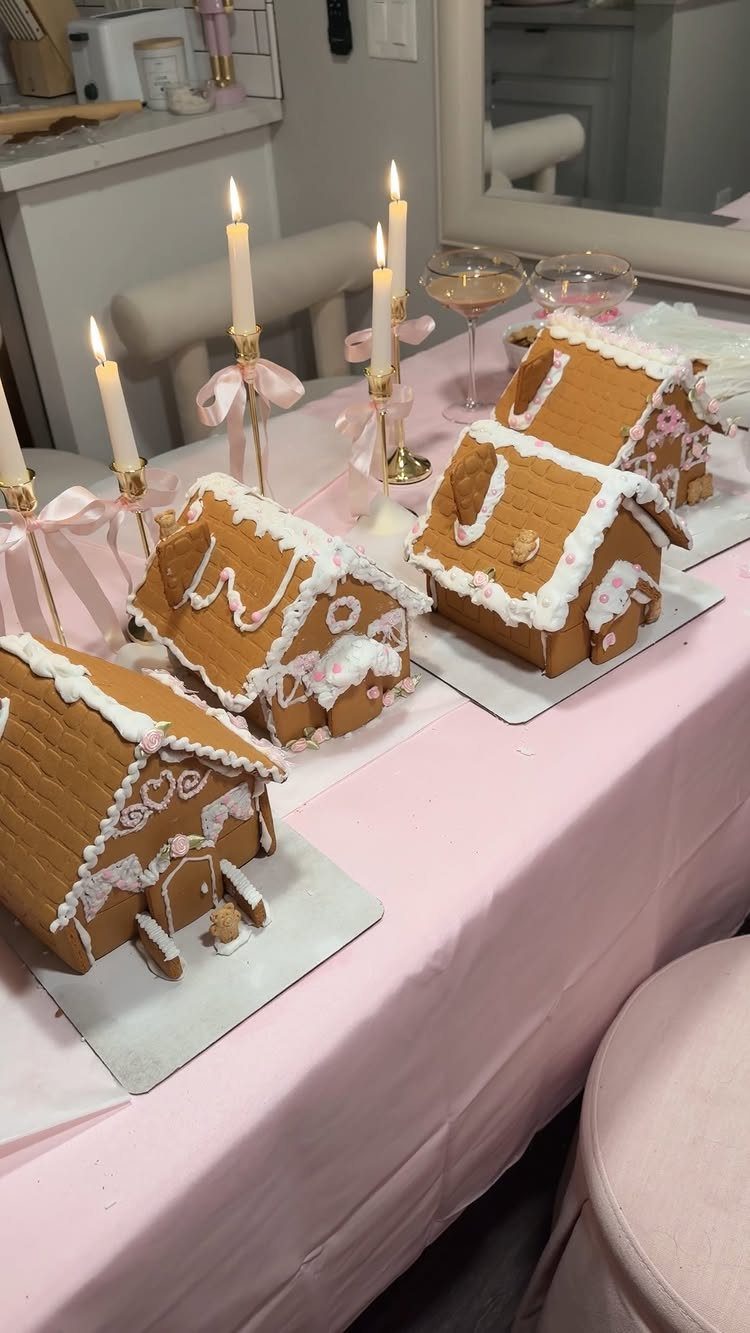 Gingerbread houses and lit candles on a pink tablecloth for a festive gathering.