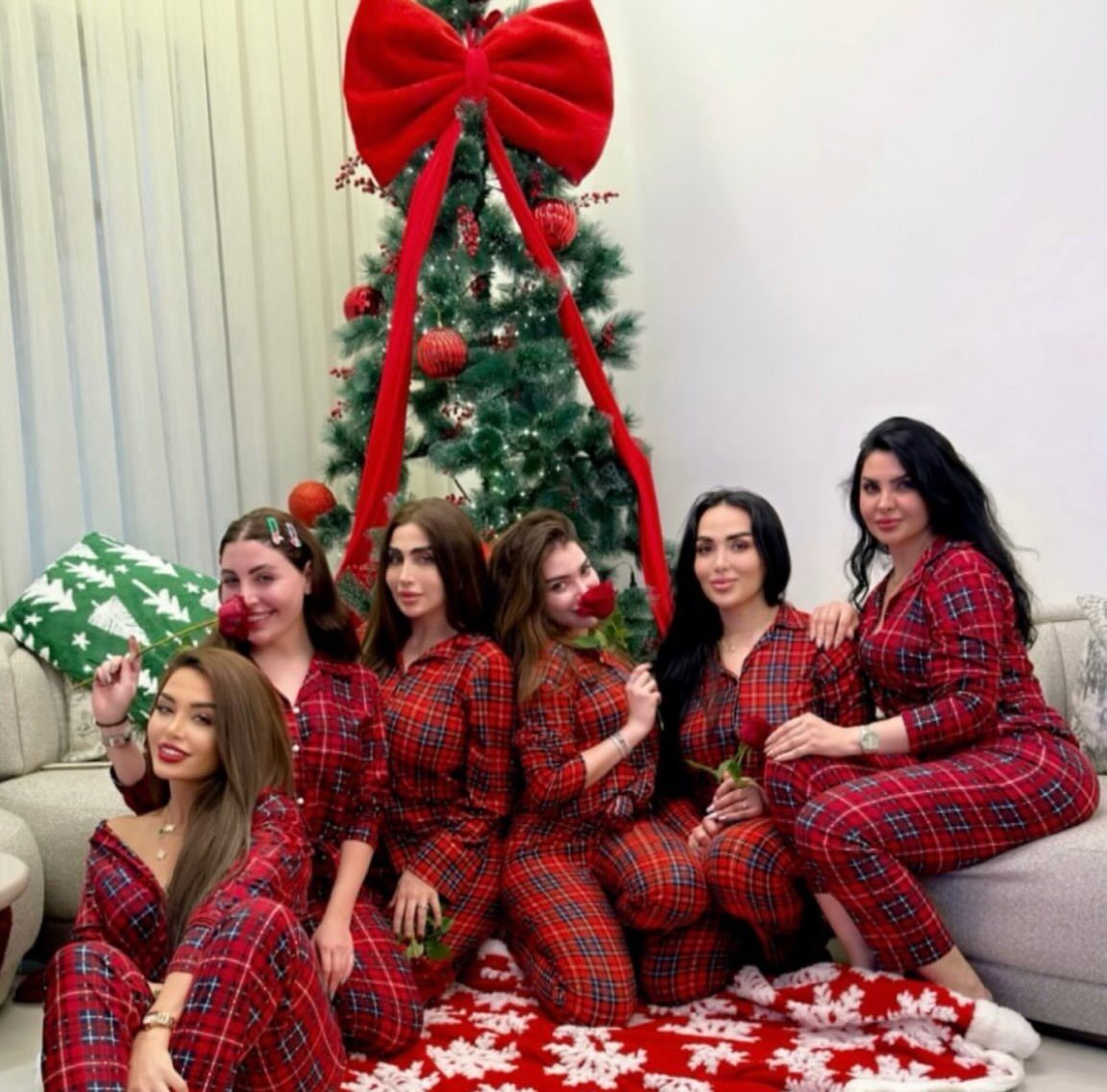 Six women in matching red plaid pajamas posing by a decorated Christmas tree.