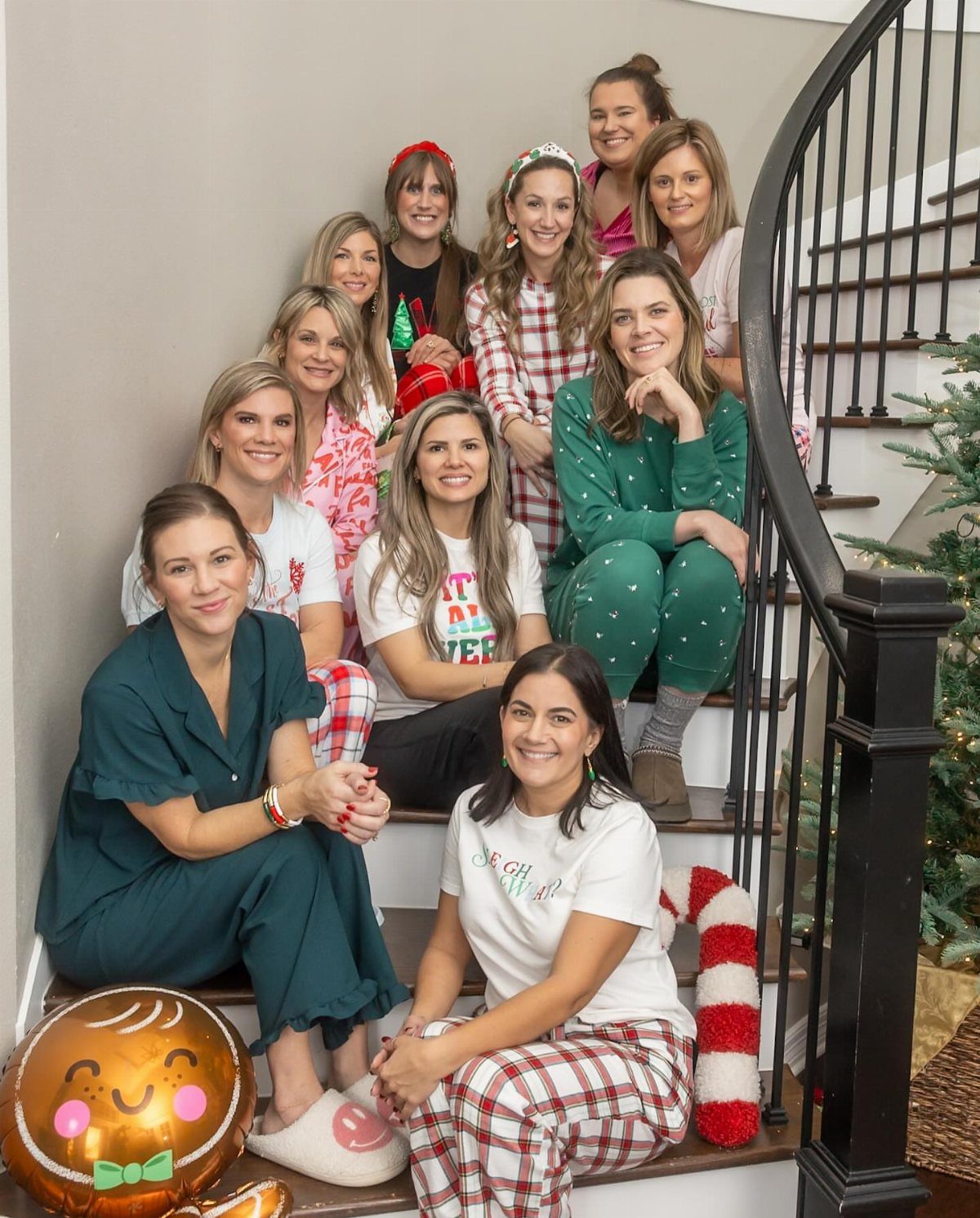 Group of women in festive pajamas posing on a white indoor staircase.