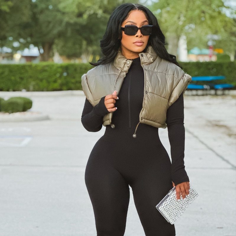 Plus-size woman in a black jumpsuit, gold puffer vest, and silver clutch bag.