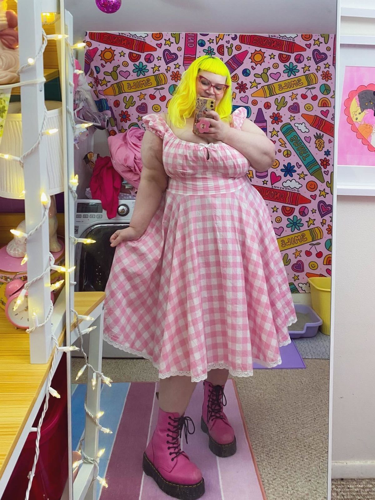 Plus-size person in a pink gingham dress and pink platform boots taking a selfie.