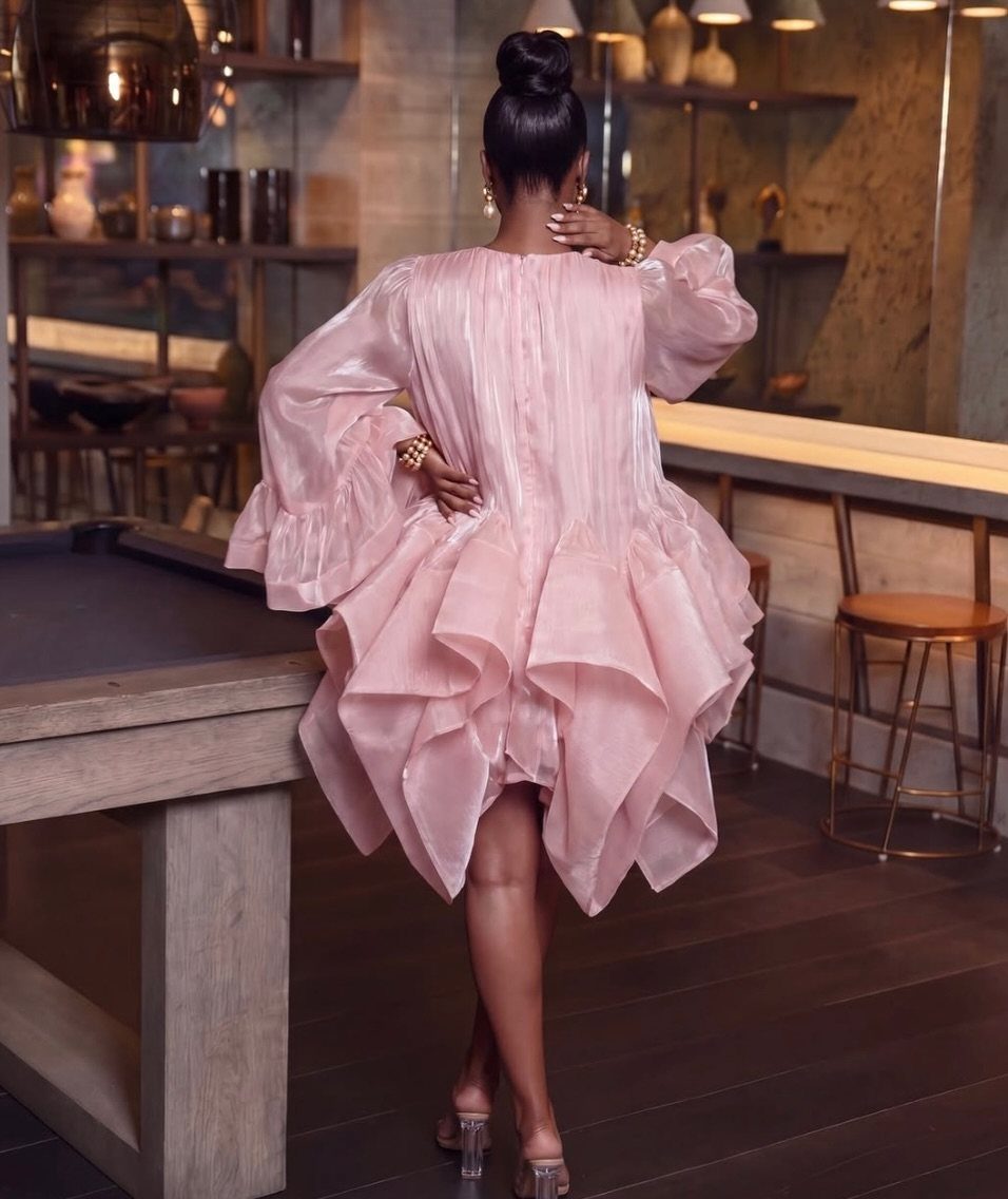 Plus-size woman in a voluminous light pink satin party dress standing in a lounge.