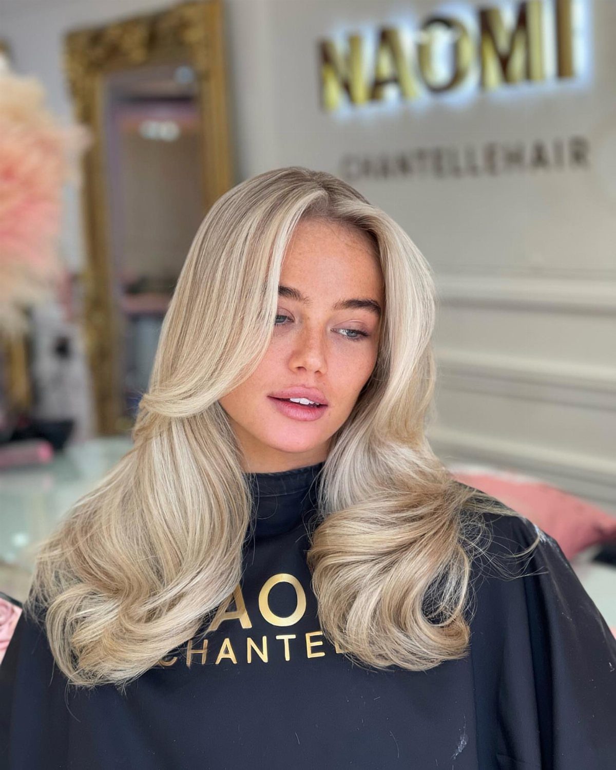 Woman with long wavy blonde hair and bright face-framing highlights in a salon.