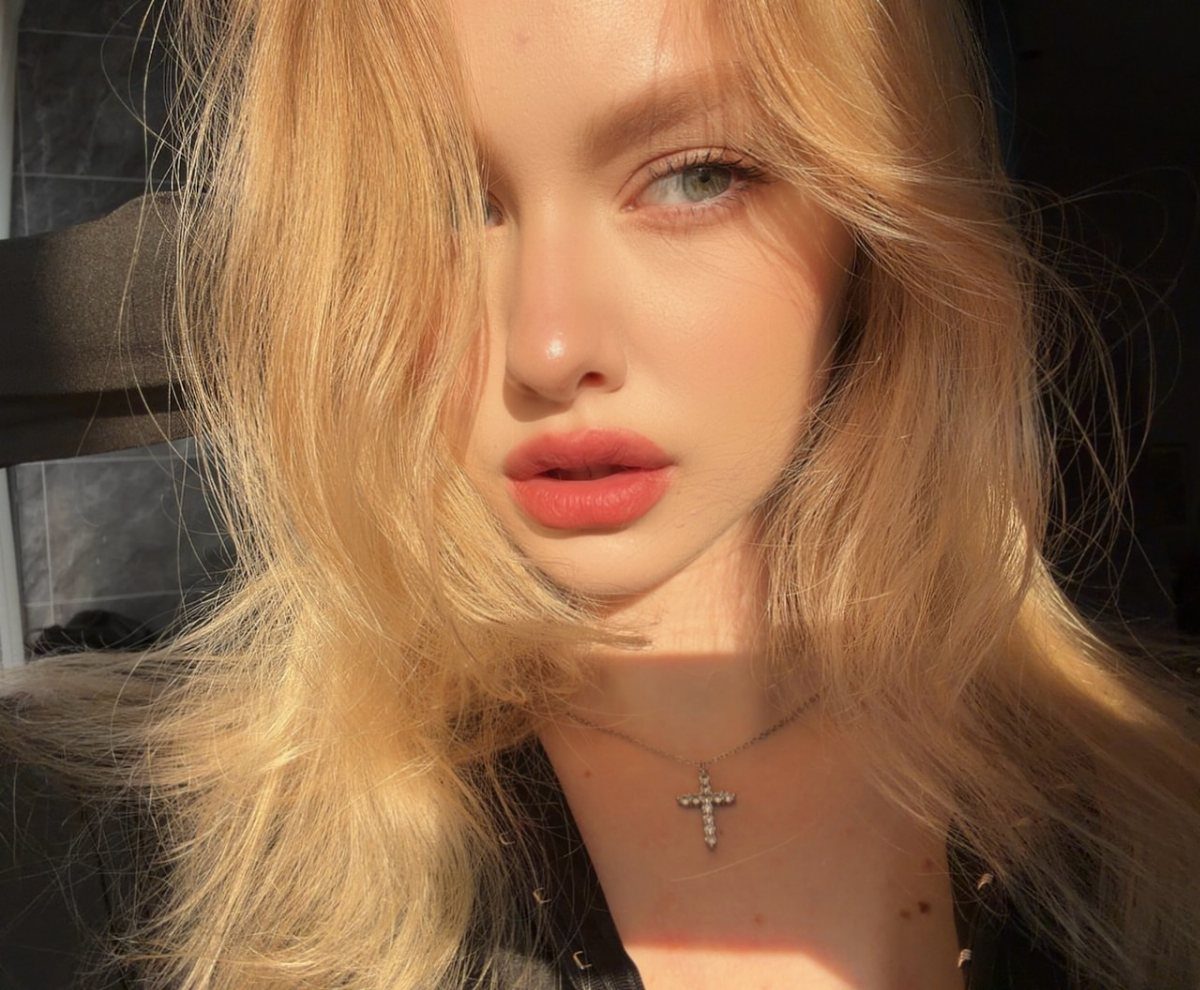 Woman with long golden blonde hair and a silver cross necklace in sunlight