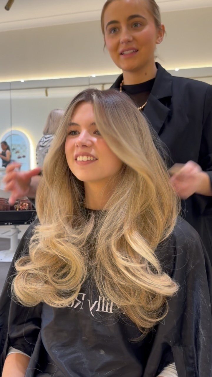 Woman with long wavy honey blonde hair smiling in a bright hair salon