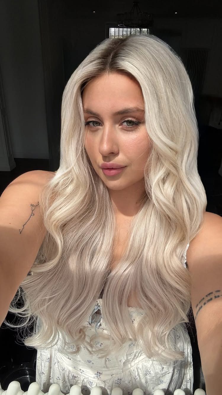 Woman with long, wavy platinum blonde hair wearing a white floral top.