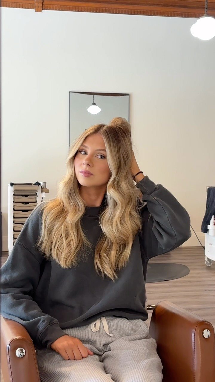 Woman with rooted blonde wavy hair sitting in a professional hair salon chair.