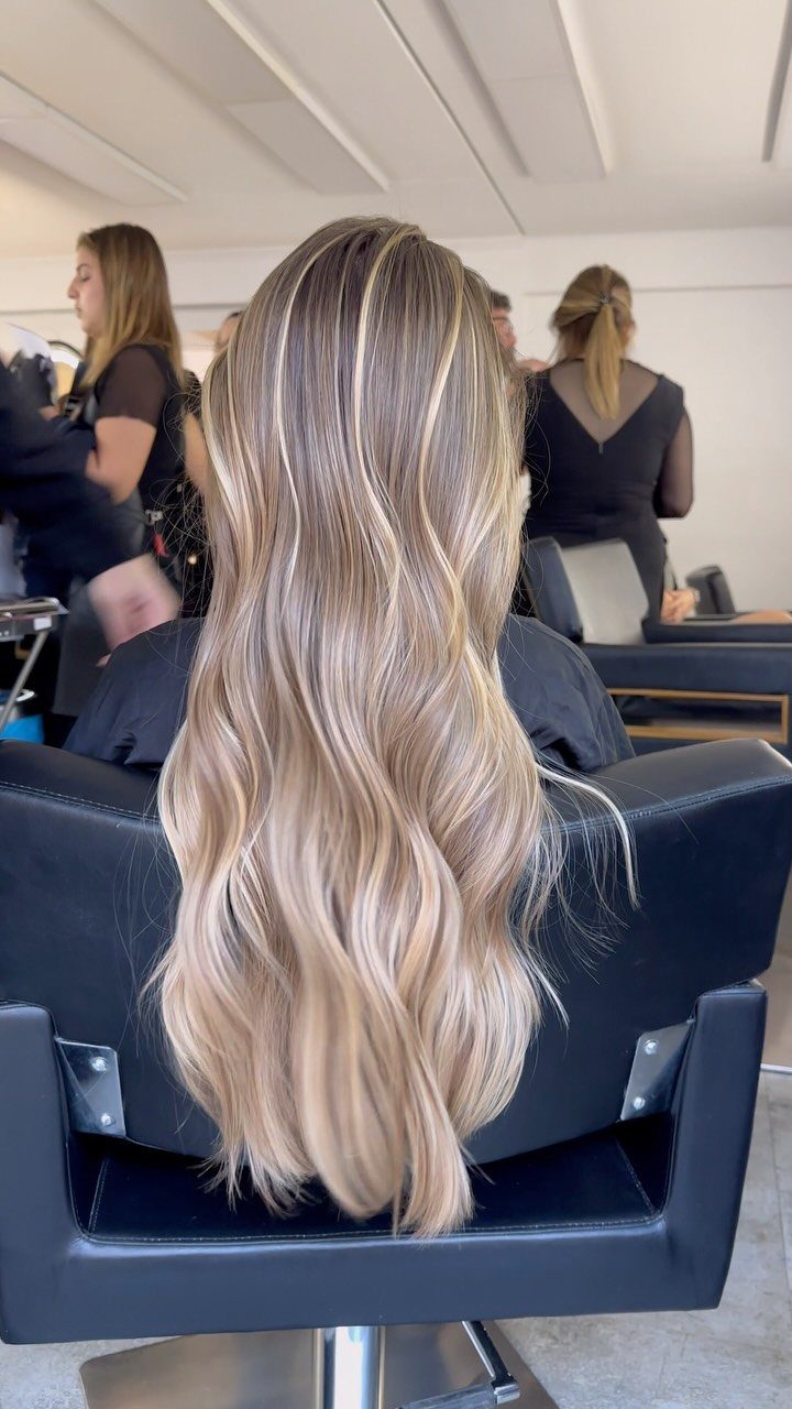 Long wavy sandy blonde hair with luminous beige tones in a salon setting