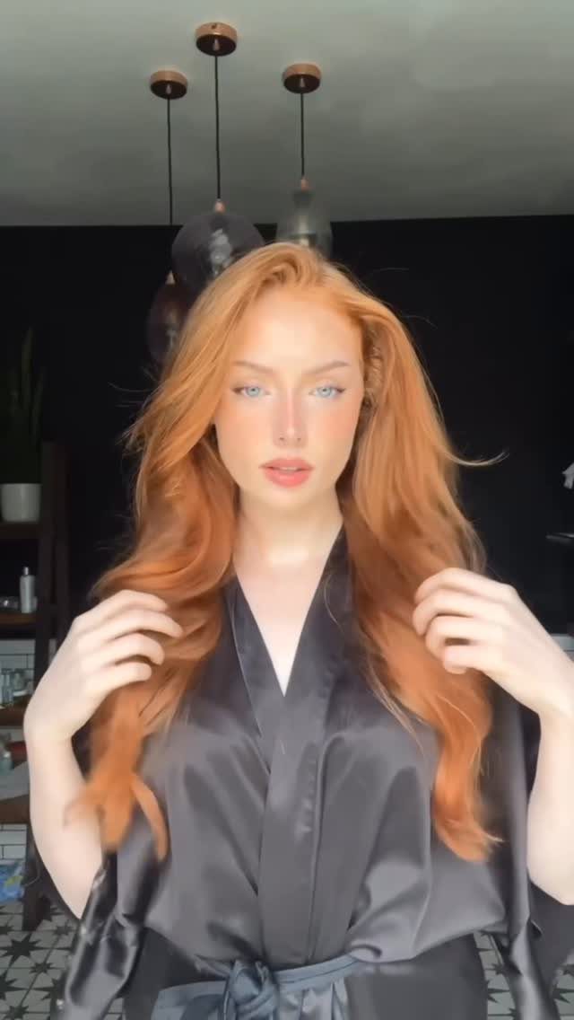 Woman with long wavy strawberry blonde hair wearing a black satin robe.