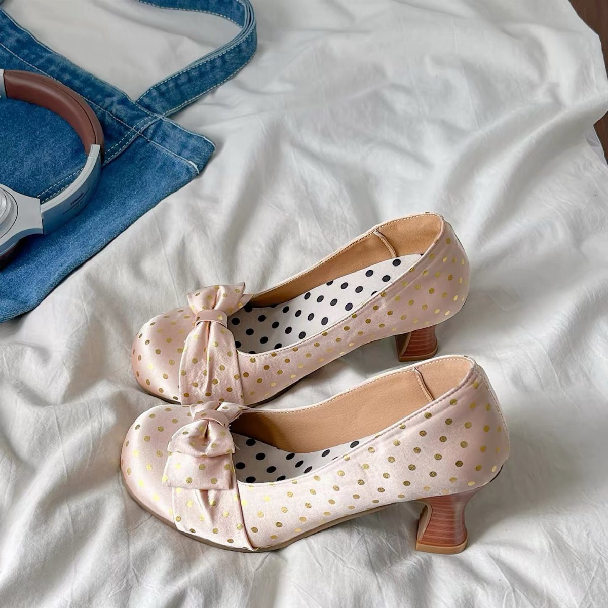 Light pink vintage heels with gold polka dots and bows on white fabric