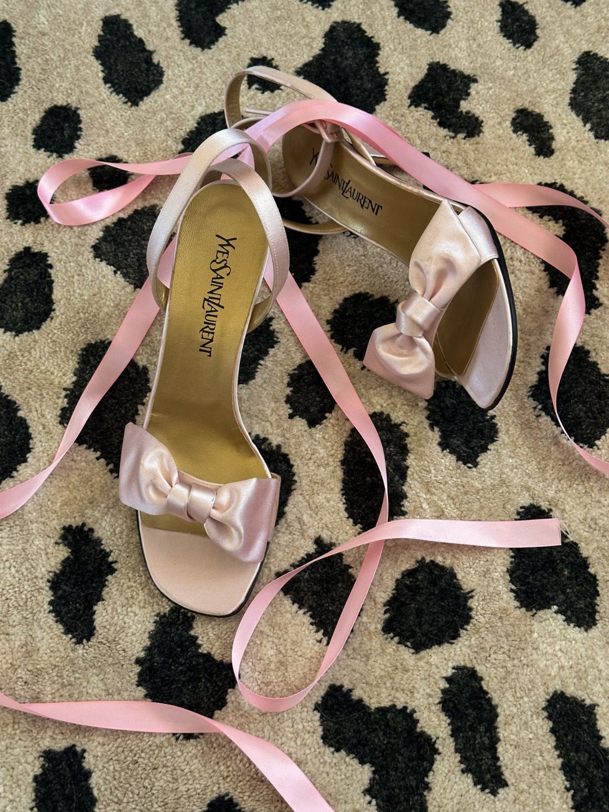Soft pink satin Yves Saint Laurent heels with bows on leopard print rug