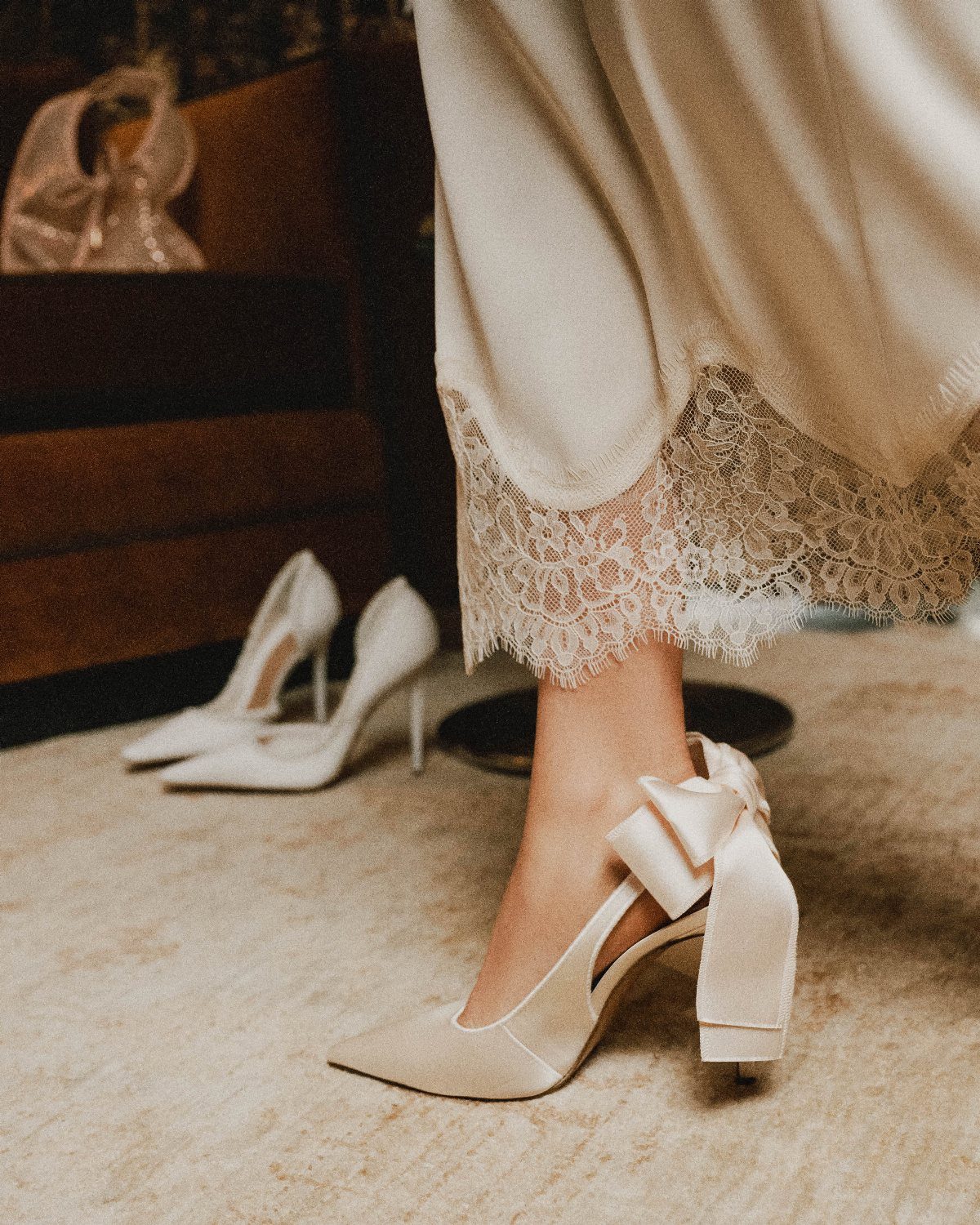 Ivory satin pointed-toe pumps with a large structural bow on the heel.