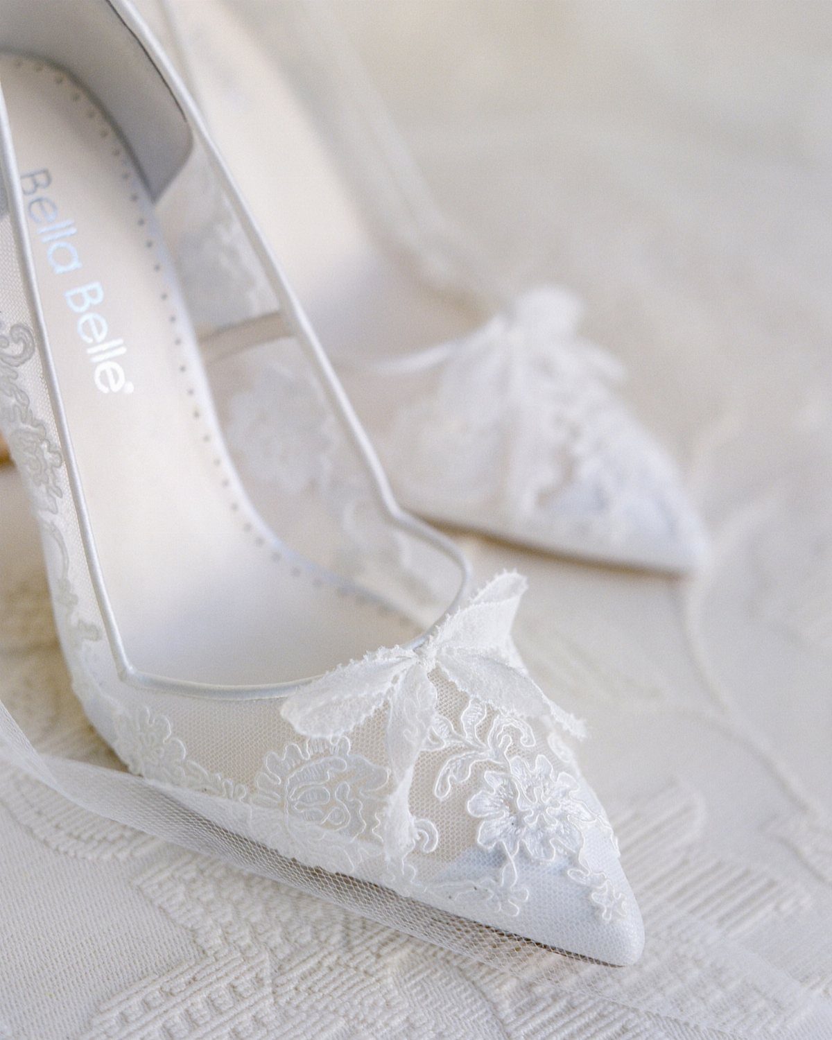 White pointed-toe pumps with floral lace overlays and a small lace bow.