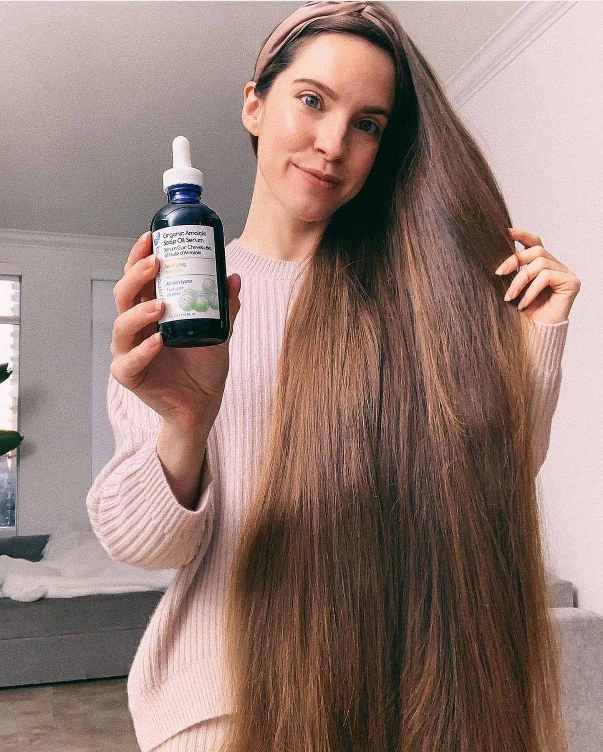 7 Products for Healthy Hair: Scalp Care to Deep Conditioners 6 Woman with long brown hair holding a small bottle of hair oil.
