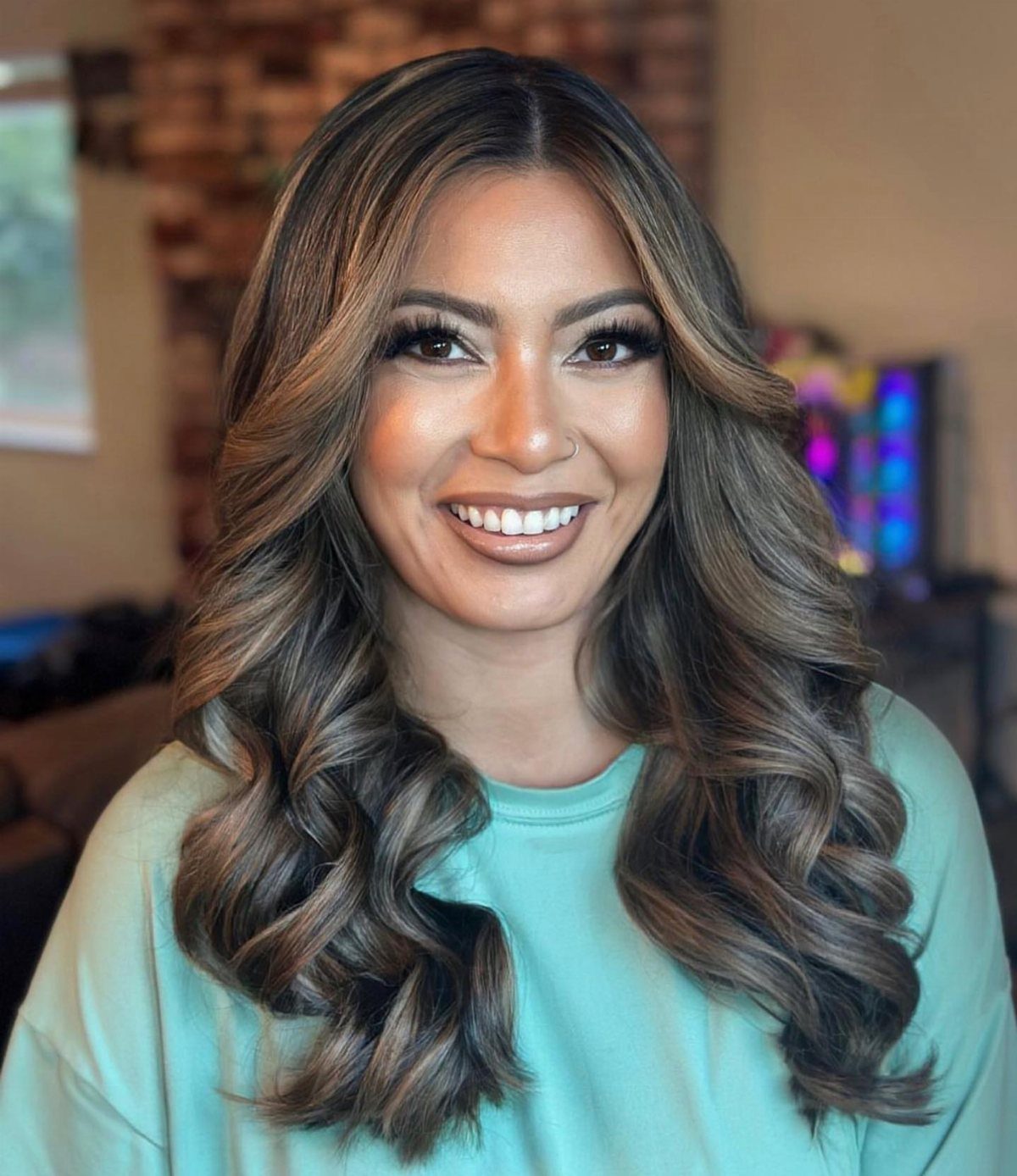 Woman with long brown hair styled in loose, voluminous curls and a smile.