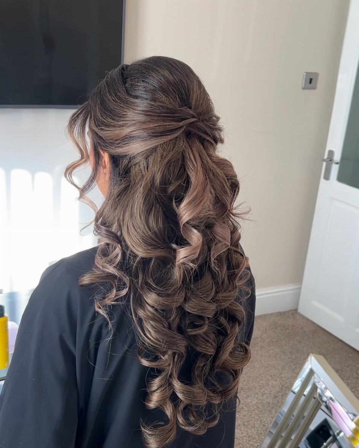 Long brown hair styled in a romantic half-up hairstyle with cascading curls.