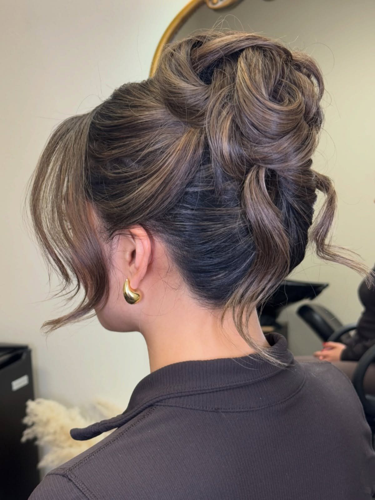 Woman with a voluminous brown textured updo and loose curling tendrils.