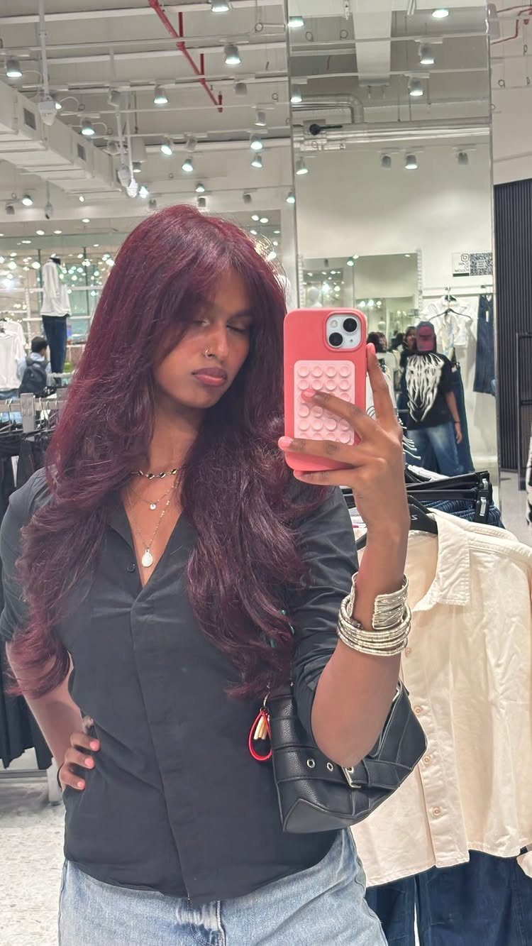 13 Red Undertones Hair Ideas, From Copper to Burgundy 12 Woman with deep red cherry cola hair taking a mirror selfie in a store