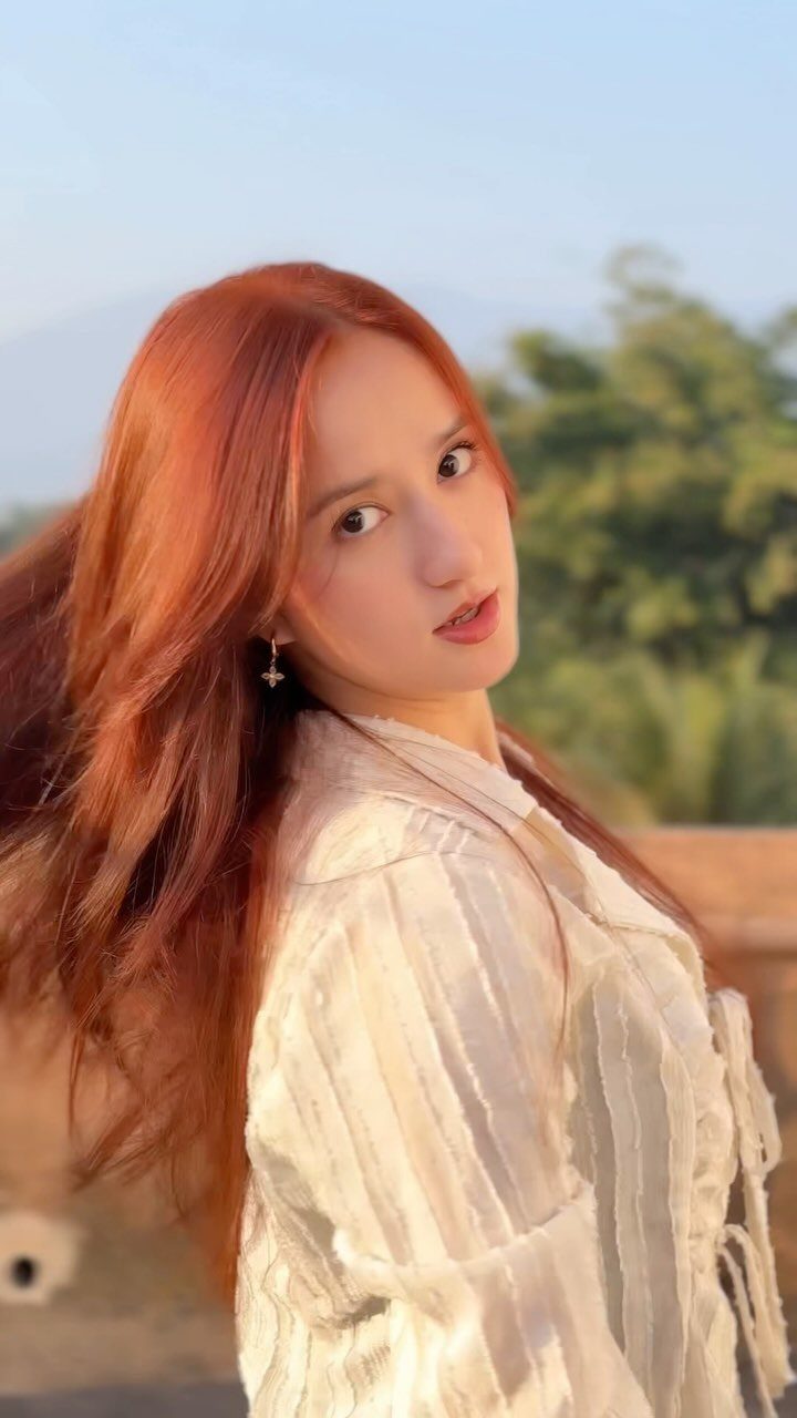 13 Red Undertones Hair Ideas, From Copper to Burgundy 5 Woman with long wavy cinnamon red hair wearing a white textured blouse outdoors.