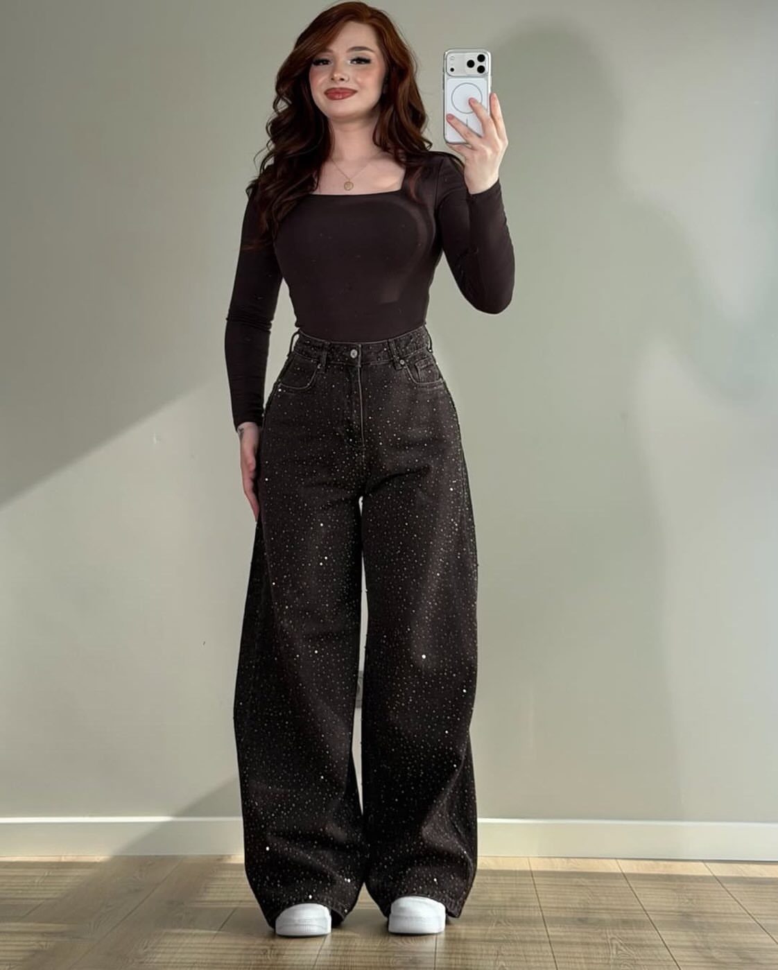 Woman wearing a black bodysuit and wide-leg black rhinestone jeans with white sneakers.