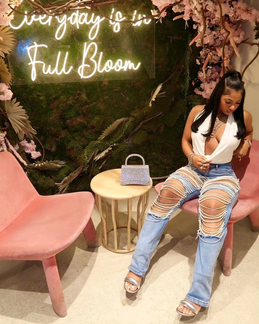 Woman wearing rhinestone embellished ripped jeans and a white sleeveless top sitting indoors.