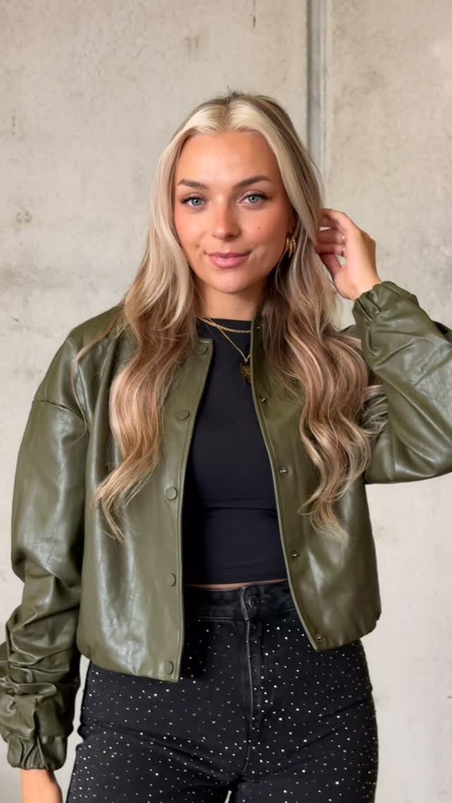 Woman wearing olive green bomber jacket and black rhinestone embellished jeans against concrete wall