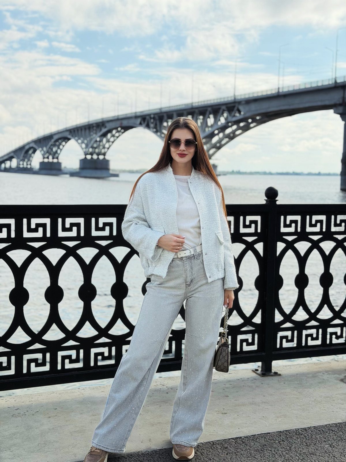Woman wearing a white tweed jacket and sparkly rhinestone wide-leg jeans by a bridge.
