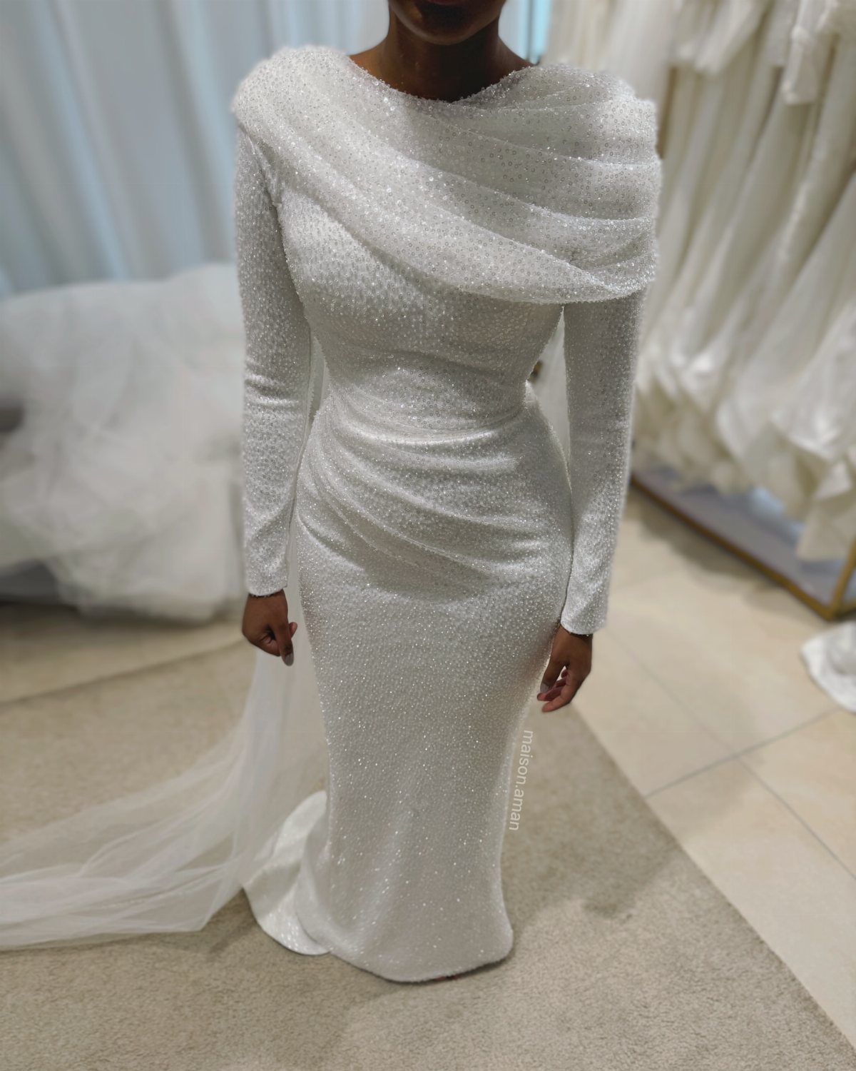 Woman wearing a shimmering white long-sleeved wedding dress in a bridal boutique.