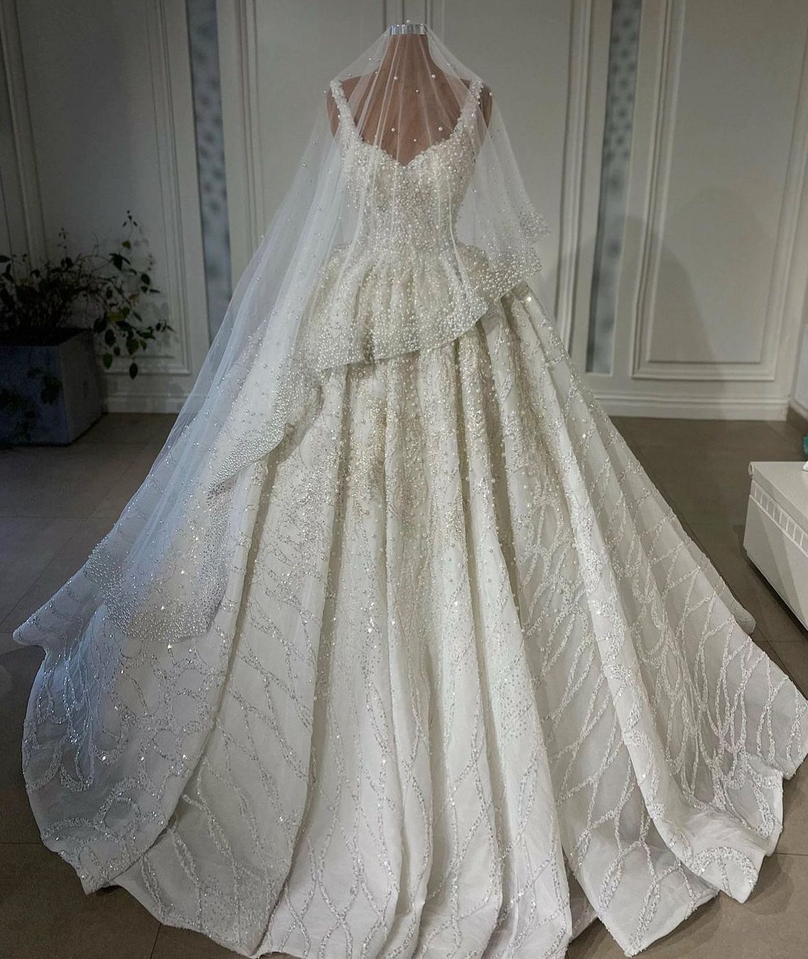 White beaded wedding dress with a long veil on a mannequin in a boutique.