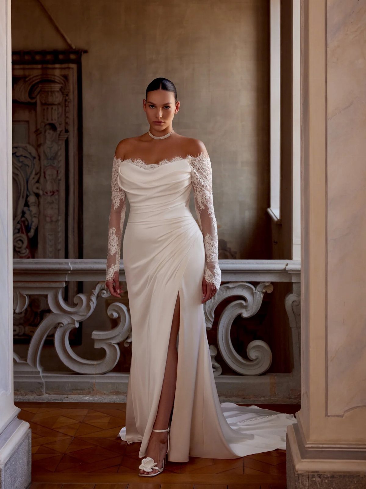 Woman in a white off-the-shoulder wedding dress with lace sleeves and high slit.