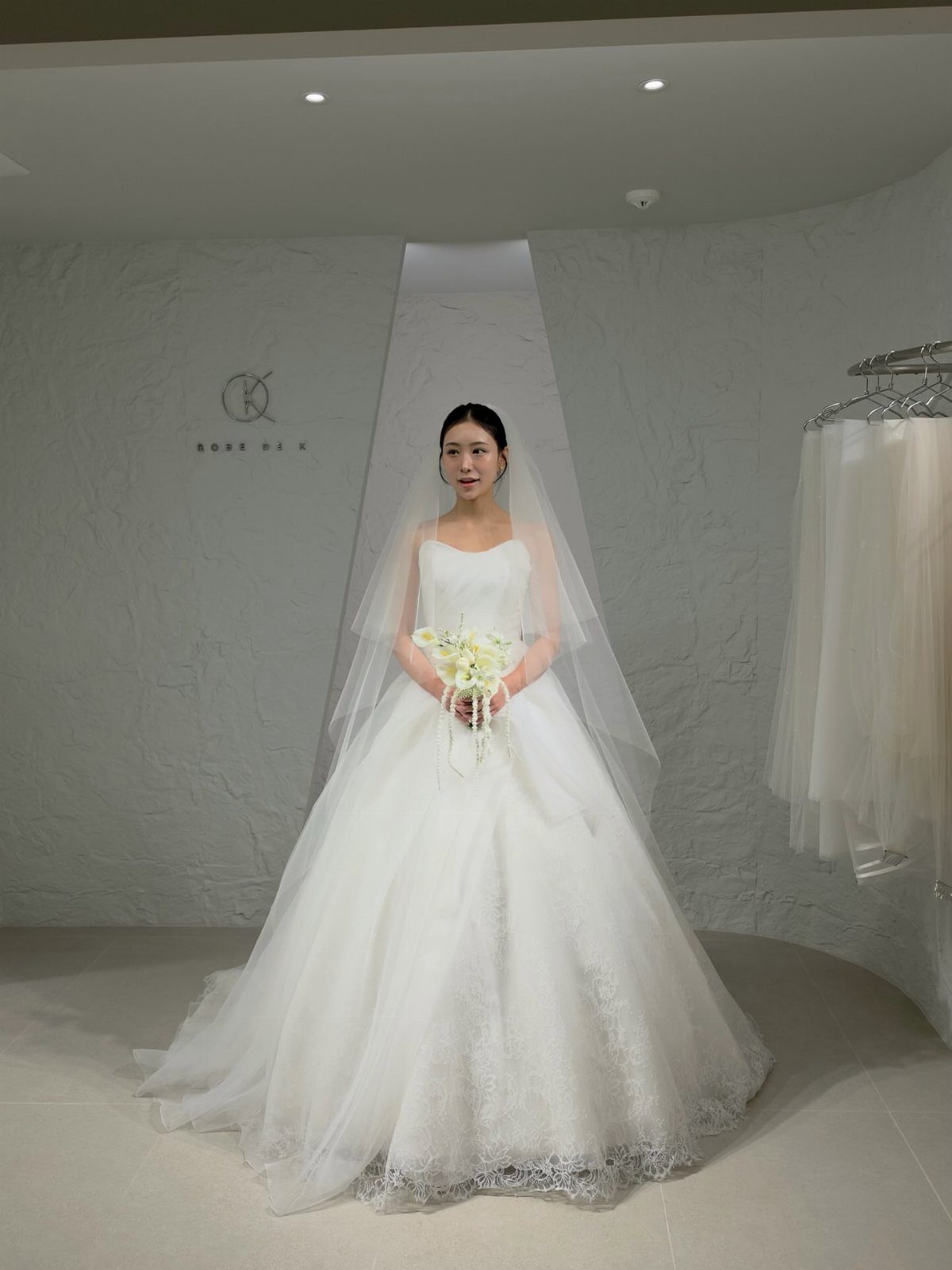 Woman in a white strapless wedding dress and veil standing in a bridal boutique.