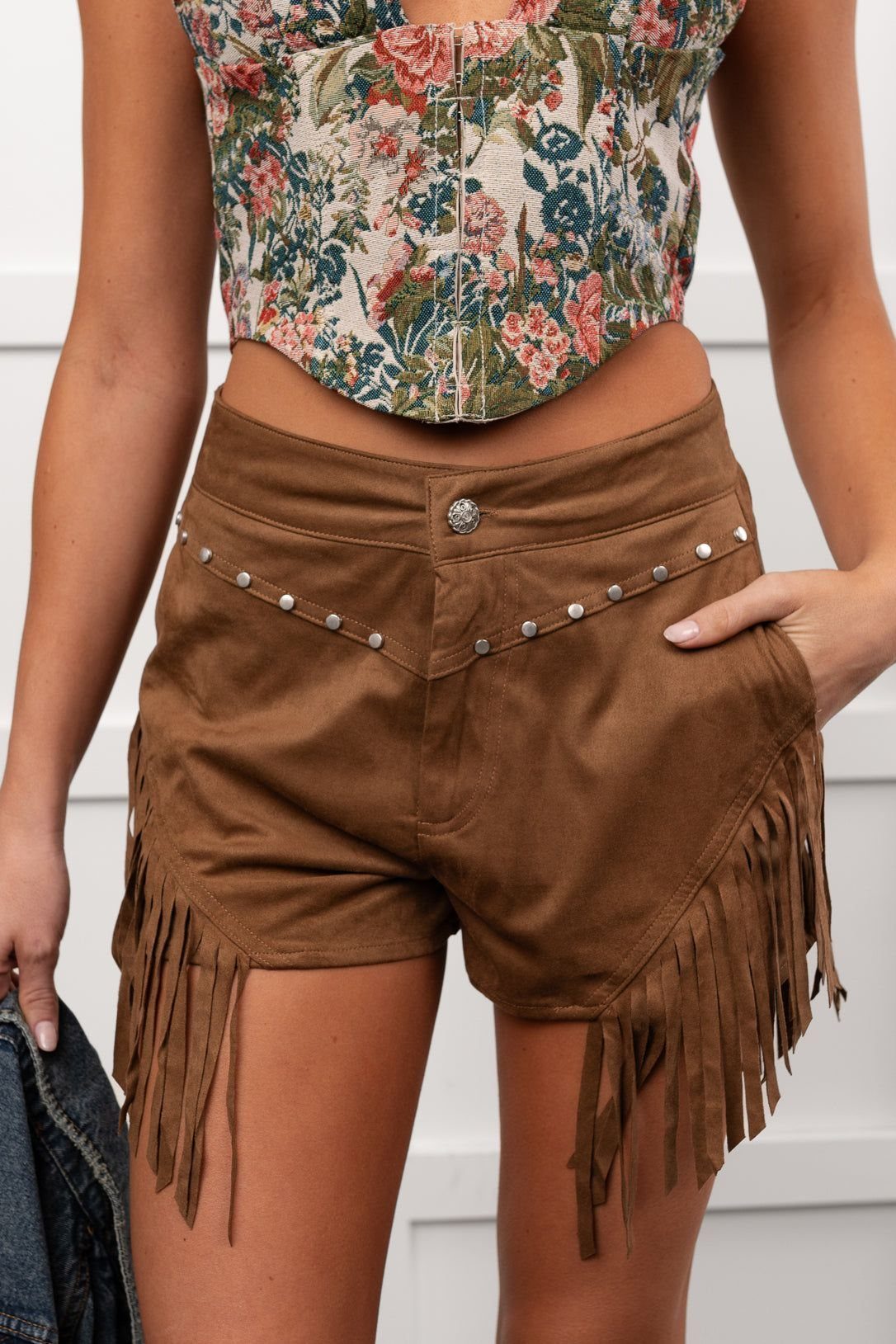 Brown faux-suede fringe shorts with silver studs paired with a floral crop top.