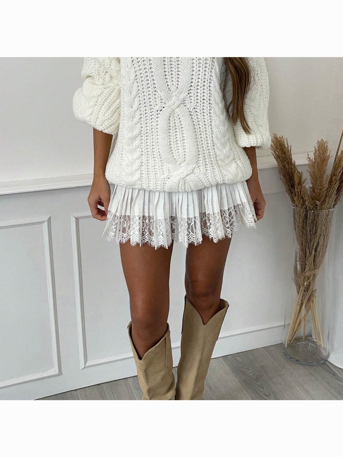 Woman wearing a white cable-knit sweater, ruffled lace mini skirt, and tan cowboy boots.