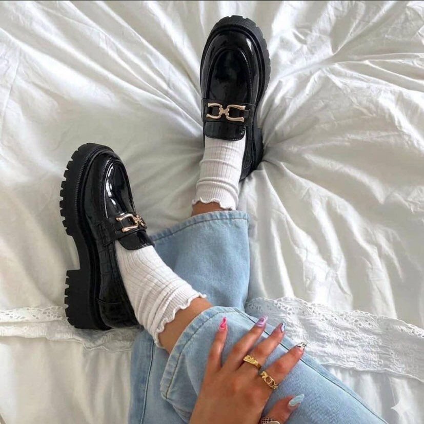 Black patent leather chunky loafers with gold hardware worn with flared blue jeans.