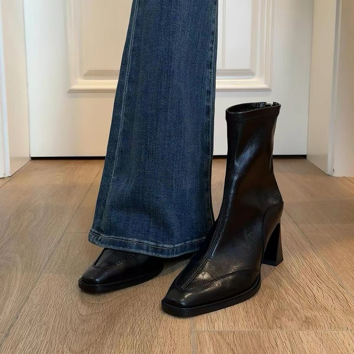 Black leather heeled boots worn with blue flared denim jeans on wooden flooring.