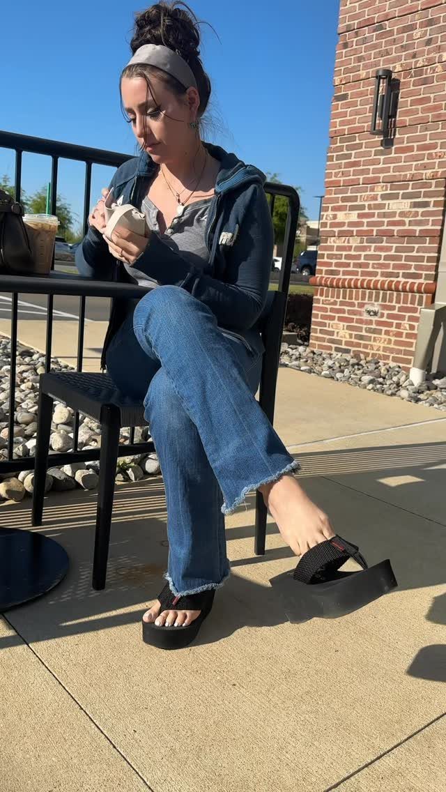 Woman wearing blue flared jeans and black platform sandals sitting outdoors.