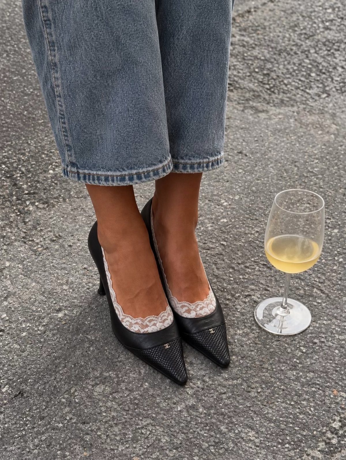 Black pointed-toe pumps with lace socks paired with blue denim jeans on asphalt.