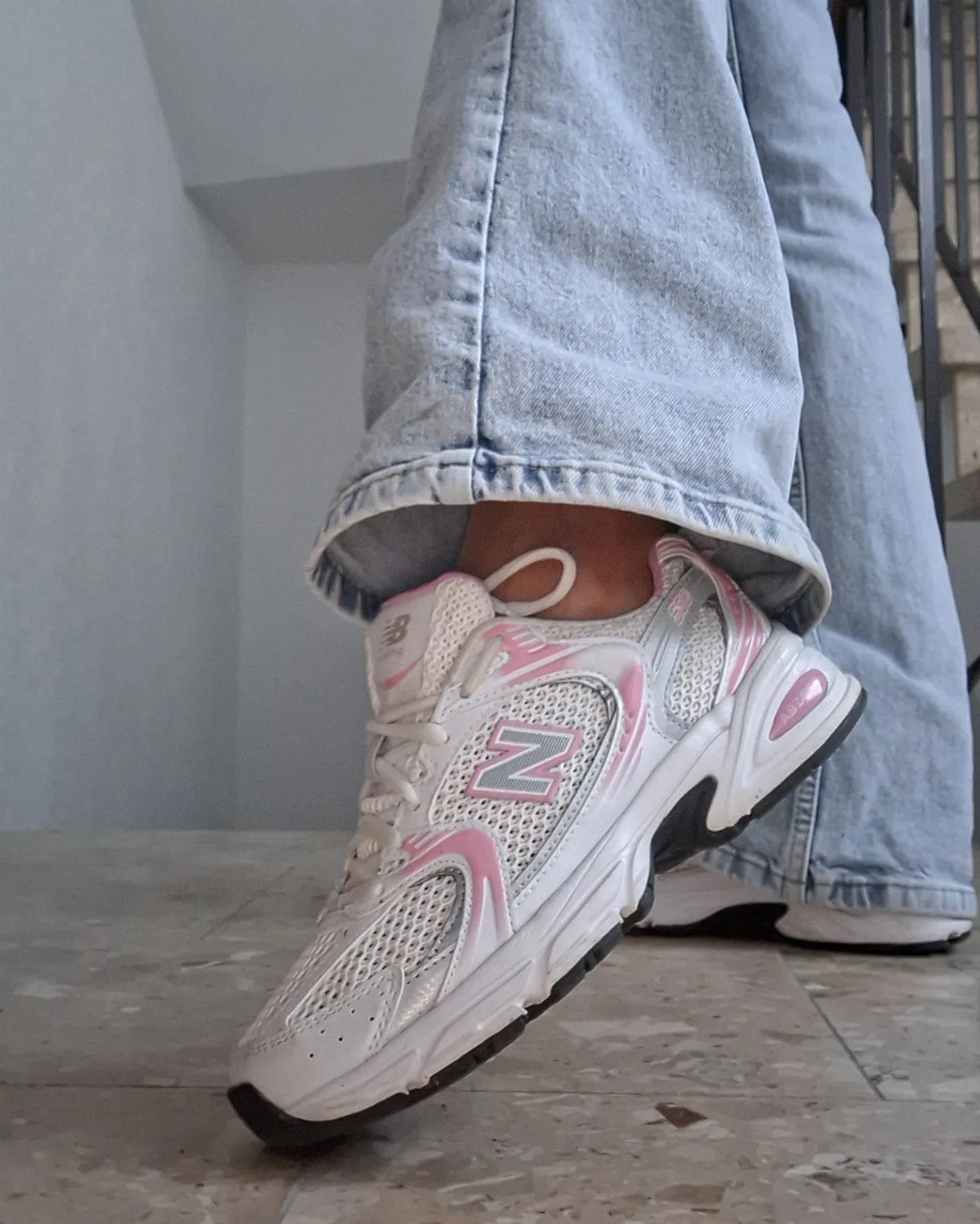 White and pink sneakers worn with light-wash blue flared jeans on stone flooring.