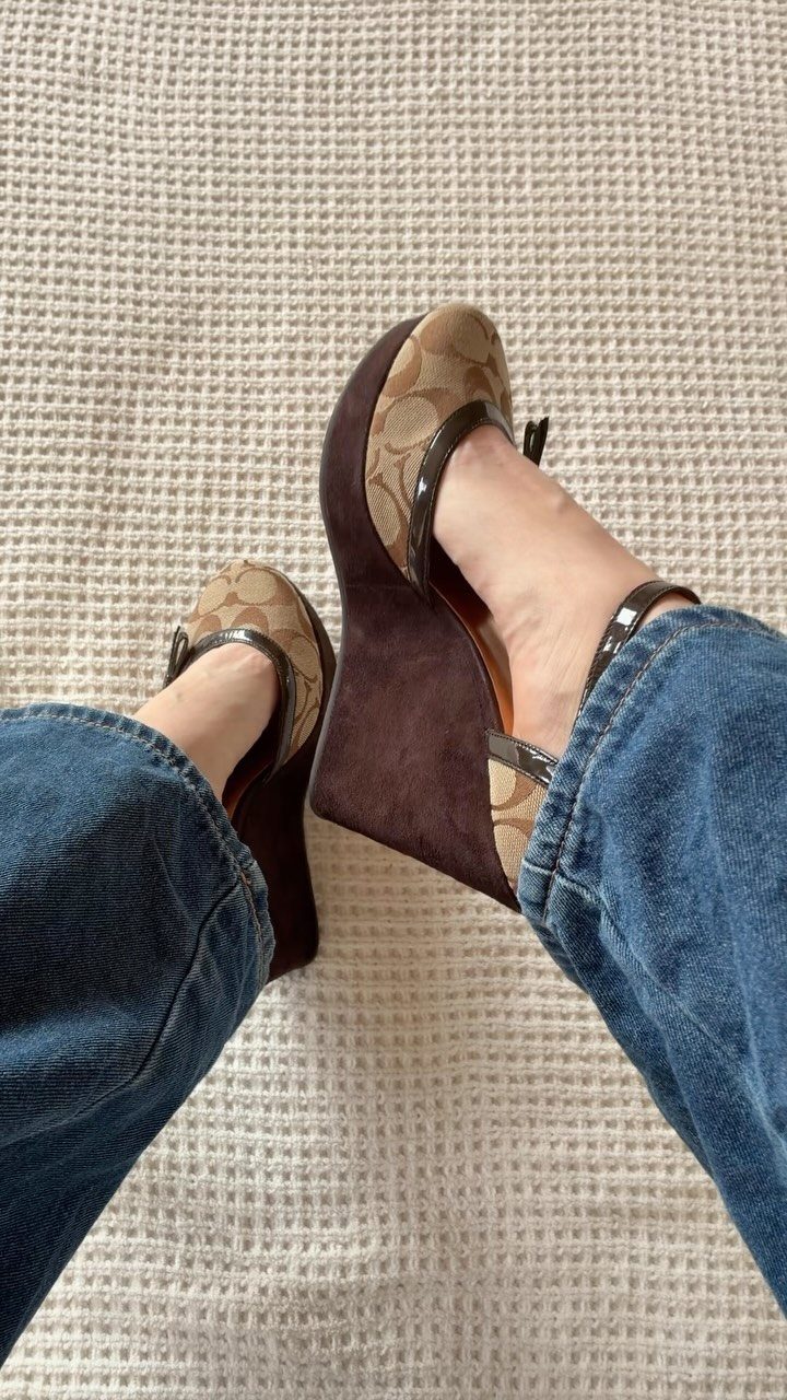 Brown patterned wedge sandals worn with blue flared jeans on a white carpet.