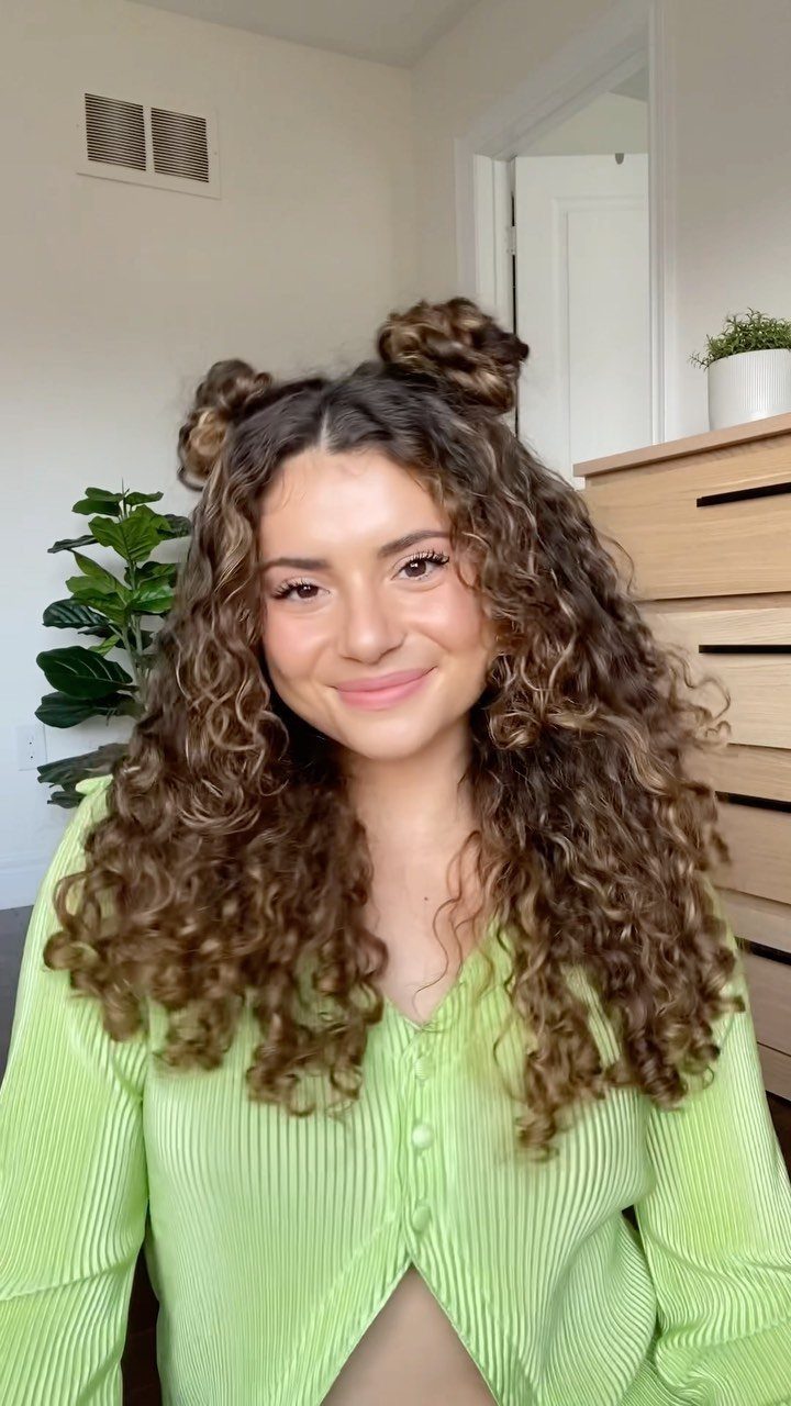 8 Simple Half Up Hairstyles for Every Occasion 7 Woman with curly brown hair styled in half-up space buns wearing green shirt.
