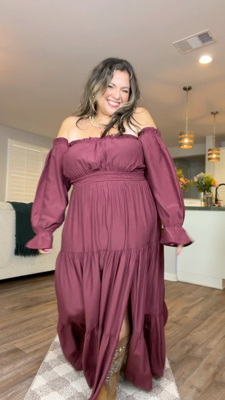 Woman in a burgundy flowy dress and tan slouchy boots in a living room