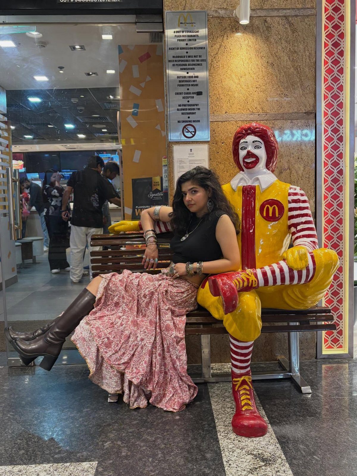 Woman in a long floral skirt and brown slouchy boots sitting by a statue.
