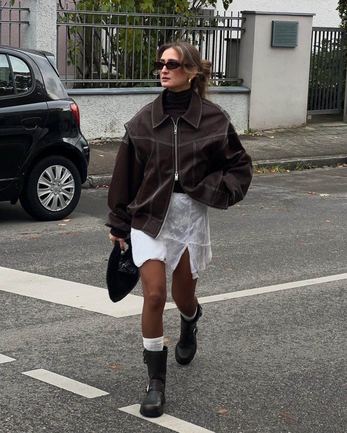 Woman in oversized brown jacket and white miniskirt wearing black slouchy boots.