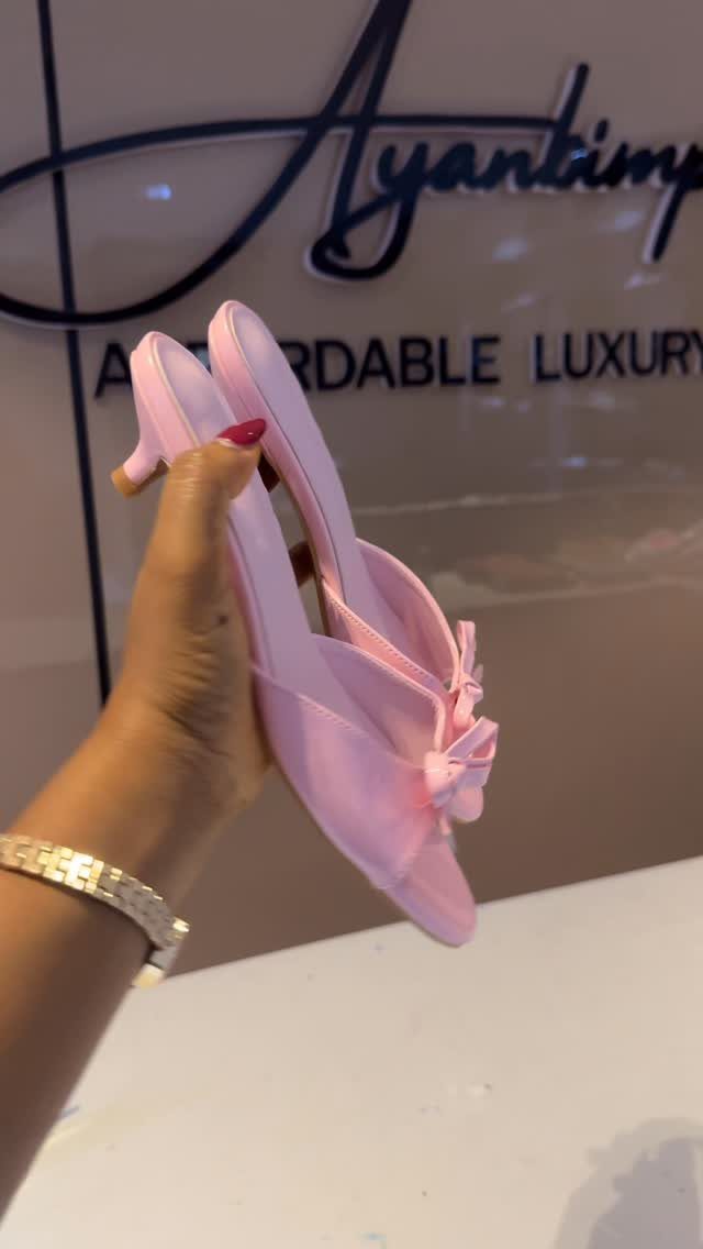 Light pink kitten heel sandals with bows held by a person's hand.