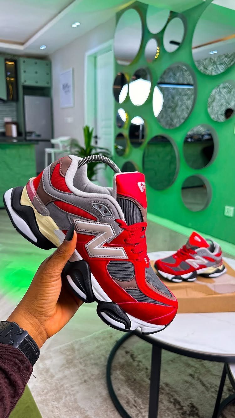 Red and grey New Balance sneakers held in a hand in a modern room.